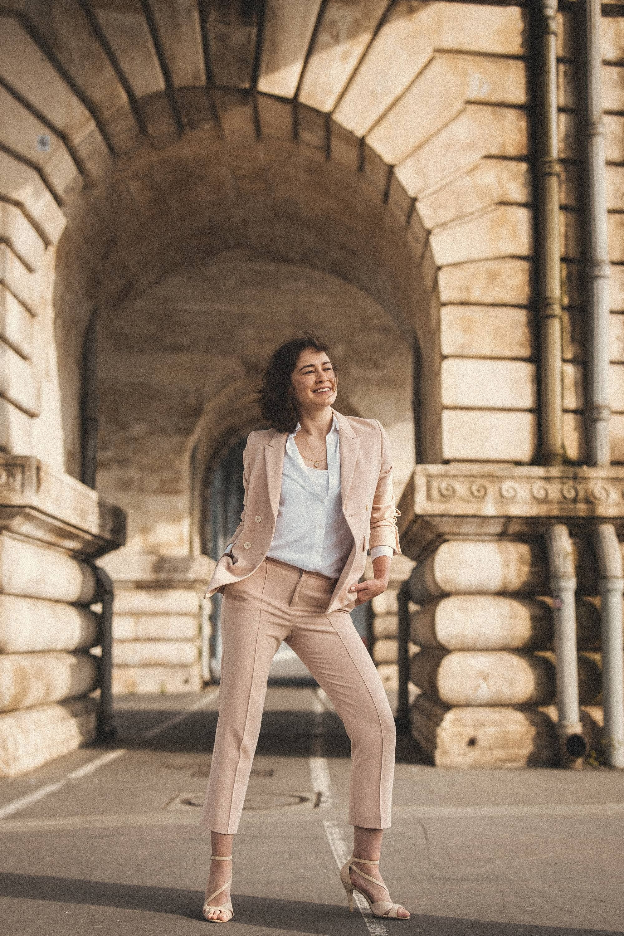 Aliya standing under a stone arch in Paris, full length